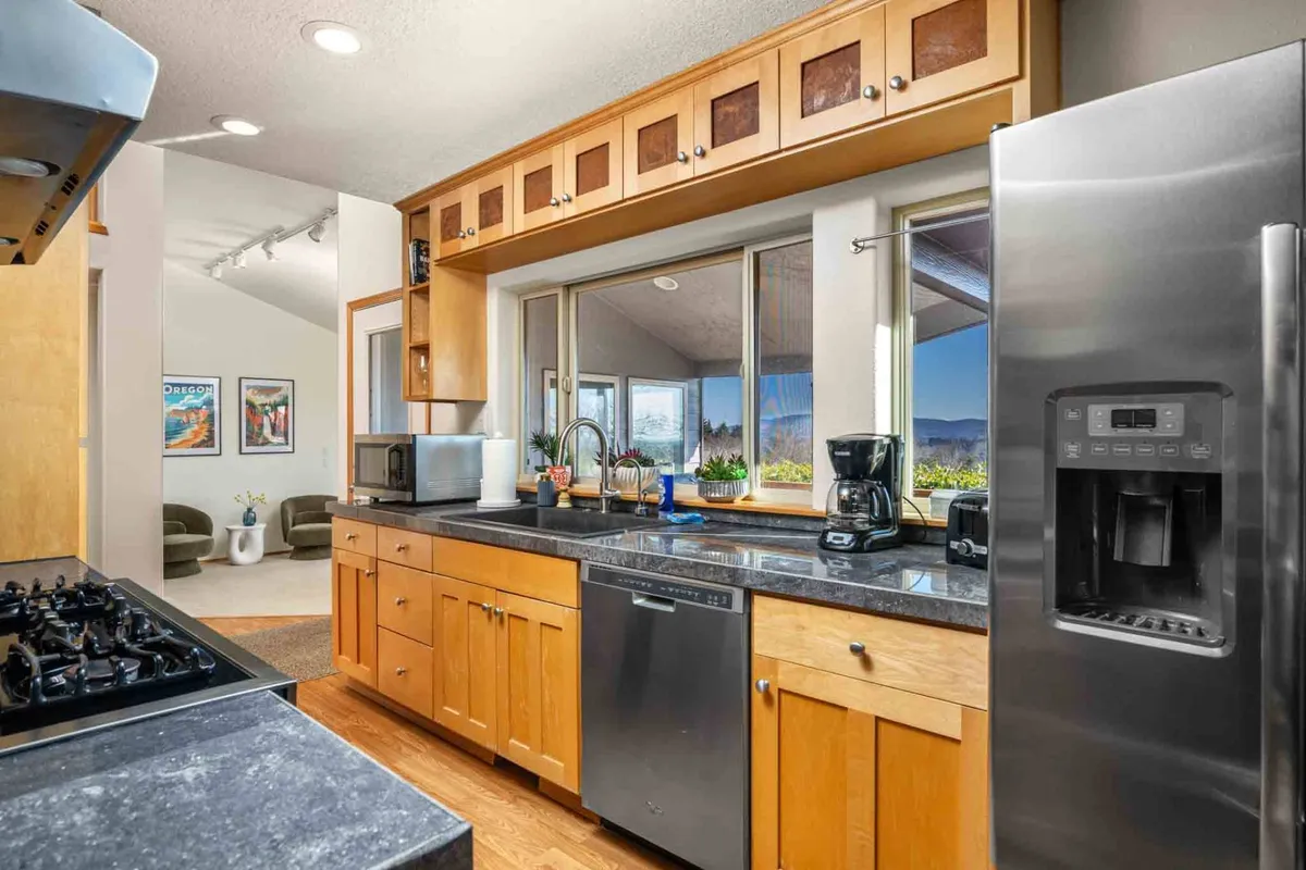 A bright, welcoming kitchen featuring a central island, stainless steel appliances, warm wood cabinetry, and a picturesque window view. The setup is ideal for cooking, entertaining, and sharing meals while still enjoying the scenery.