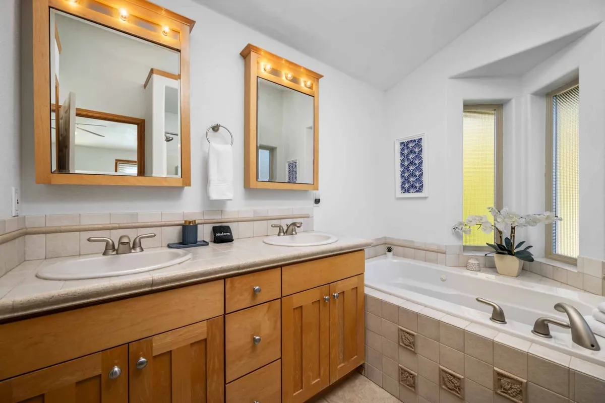 A bright, spa-like bathroom complete with a double sink vanity, mirrors, and a bathtub beside a window. Natural light pours in, creating an inviting space for relaxation and personal care.