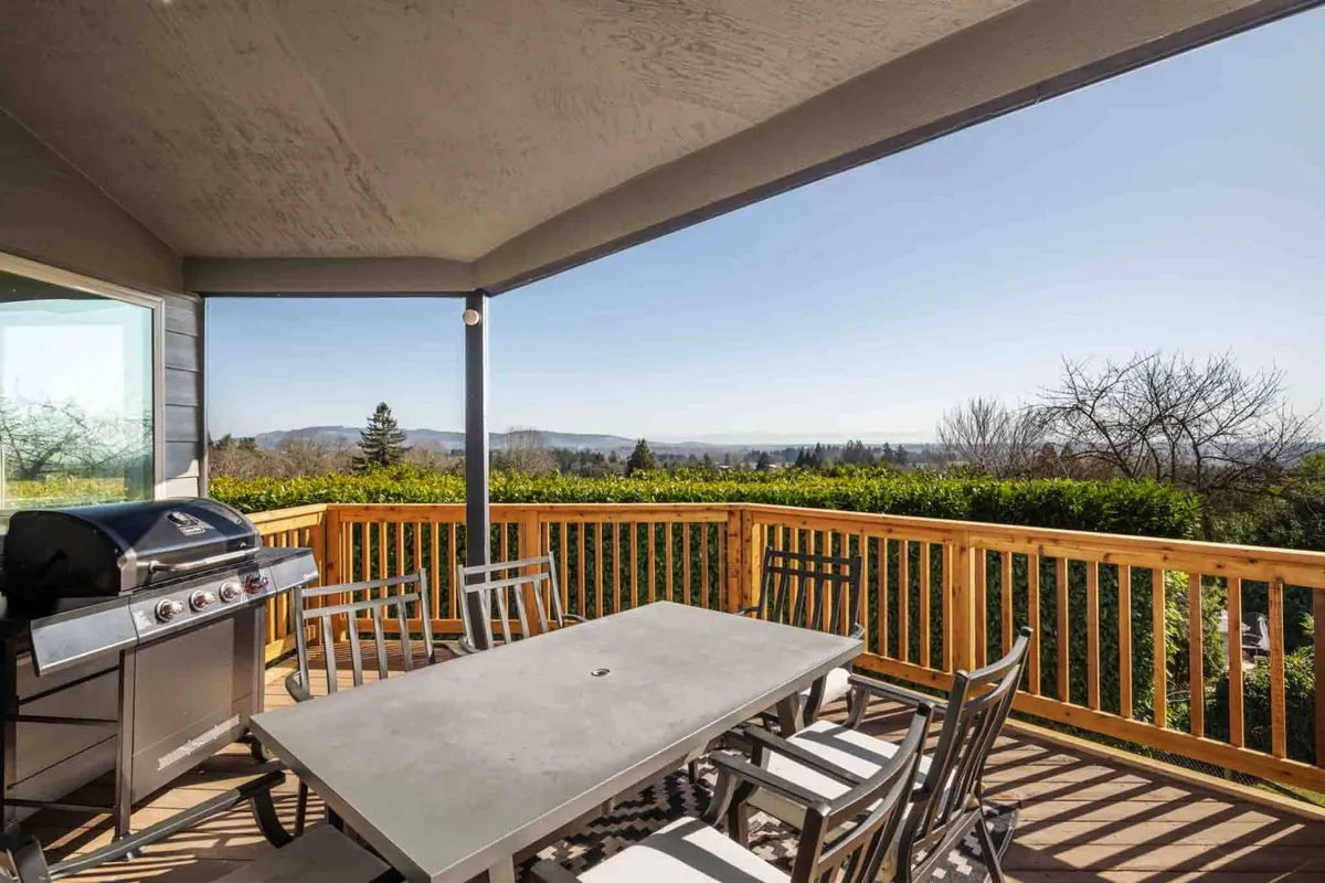 An outdoor covered deck with plush seating, a BBQ grill, dining table, and stunning views of the surrounding landscape. The scene invites guests to enjoy sunset toasts or peaceful morning coffees above the vineyards.