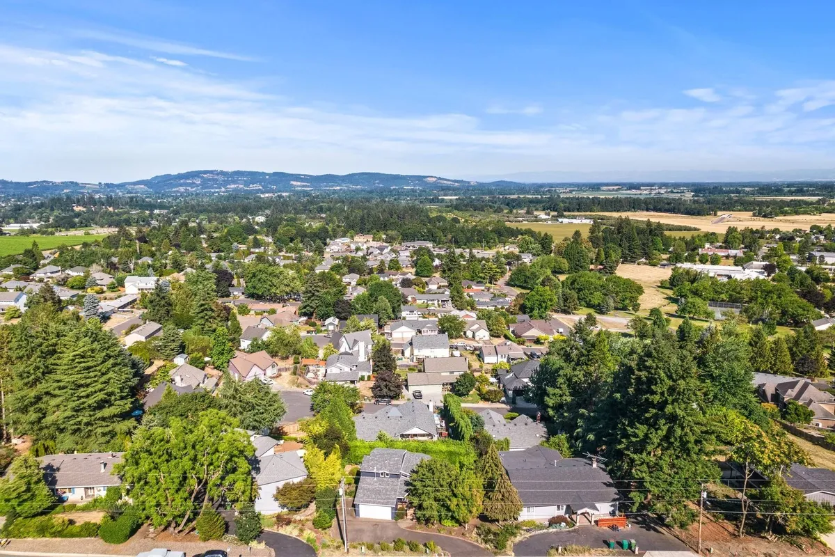 This neighborhood view shows residential houses nestled among green trees and open fields, conveying a peaceful, family-friendly community setting. The open space and proximity to nature evoke opportunities for outdoor exploration and walks to local parks.