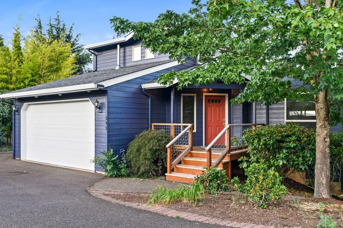 This exterior image features the inviting red front door of Dogwood Villa, with wooden steps leading up to the entrance. The green foliage and a glimpse of the garage hint at the home's spaciousness and suitability for family gatherings. The scene suggests a welcoming arrival point and outdoor areas ideal for activities.