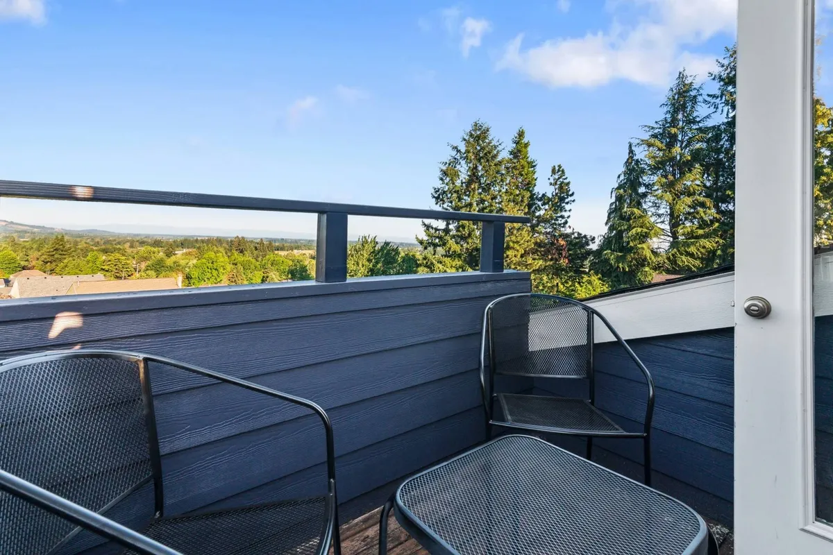 A serene balcony scene featuring comfortable seating overlooking lush green trees and a distant landscape. The image evokes a sense of relaxation and connection with the outdoors, with ample space for group gatherings or quiet reflection. The soft lighting suggests a tranquil environment ideal for unwinding or informal conversations.