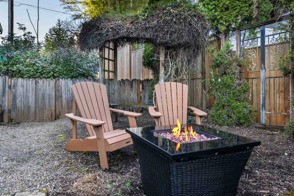 An exterior view of the backyard features a fire pit surrounded by Adirondack chairs beneath an overhead trellis. The setup invites guests to enjoy relaxed, memorable evenings outdoors.