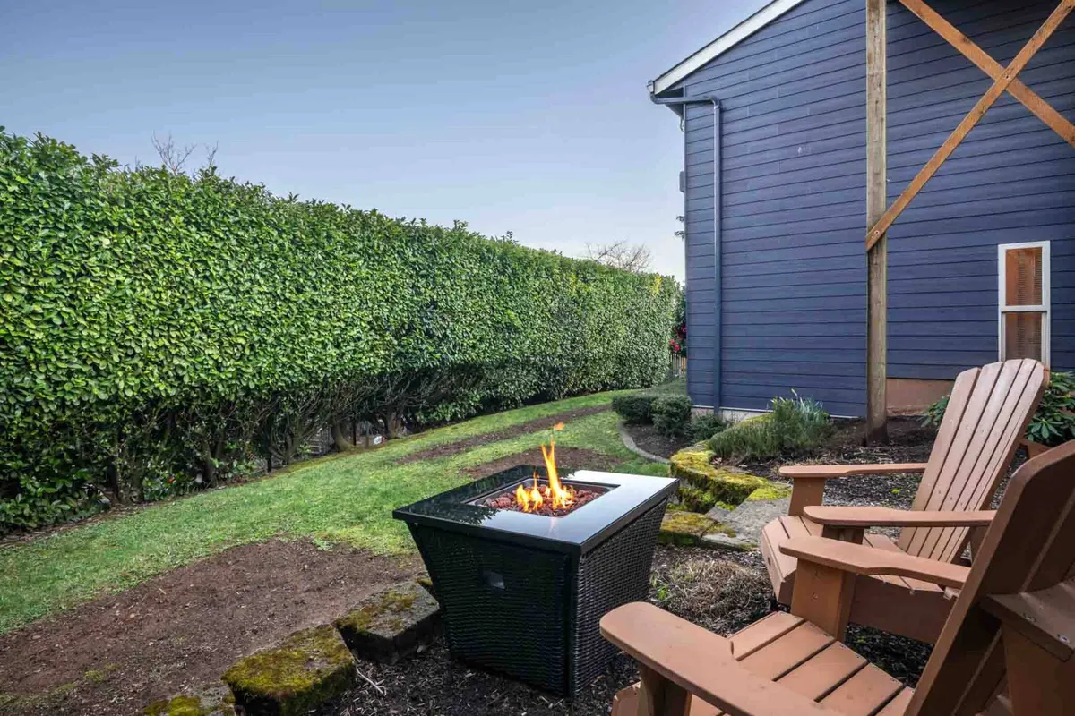 An outdoor fire pit is surrounded by Adirondack chairs and bordered by a lush green hedge. The setup is perfect for cozy storytelling, s'mores, and intimate conversations under the stars.